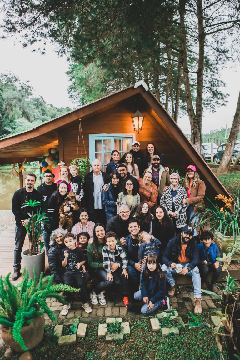 A joyful family group poses together in front of a charming wooden cabin surrounded by nature.